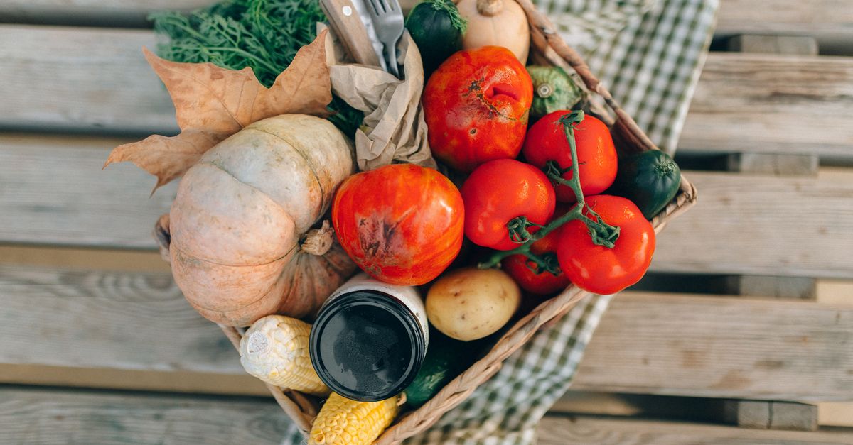 A top-down view of a basket filled with fresh vegetables and produce, placed on a wooden table.